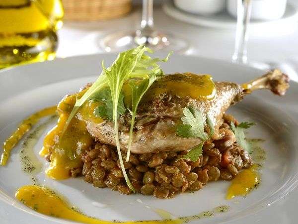 White plate with duck leg on stewed lentils