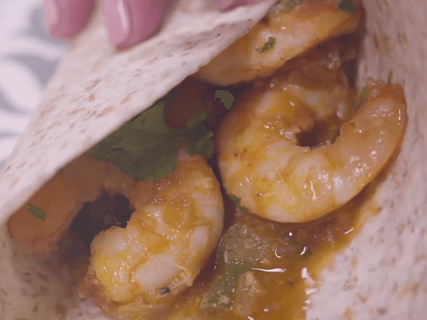Fingers taking a taco of prawns with sauce