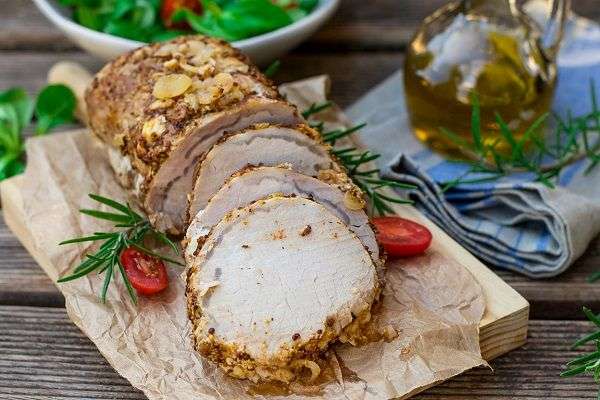 Pork loin on wooden cutting board on top of wooden table.