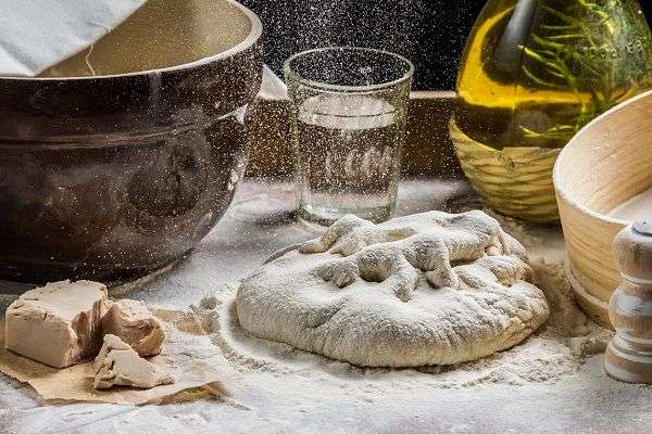 Pizza dough, yeast, bottle of oil, salt on table covered with flour